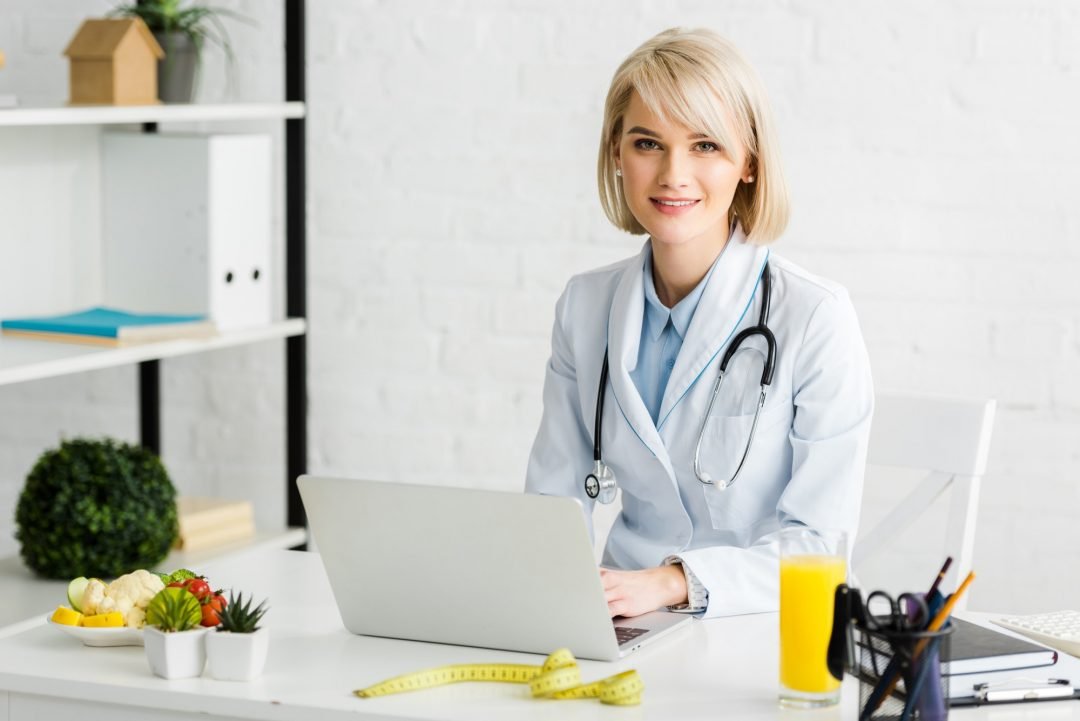 cheerful-blonde-nutritionist-sitting-near-laptop-and-glass-of-fresh-orange-juice.jpg